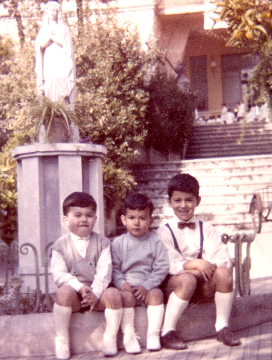 Fotografia d’epoca di tre bambini seduti davanti alla statua della Madonnina nel giardino della villa, con la scalinata alle spalle