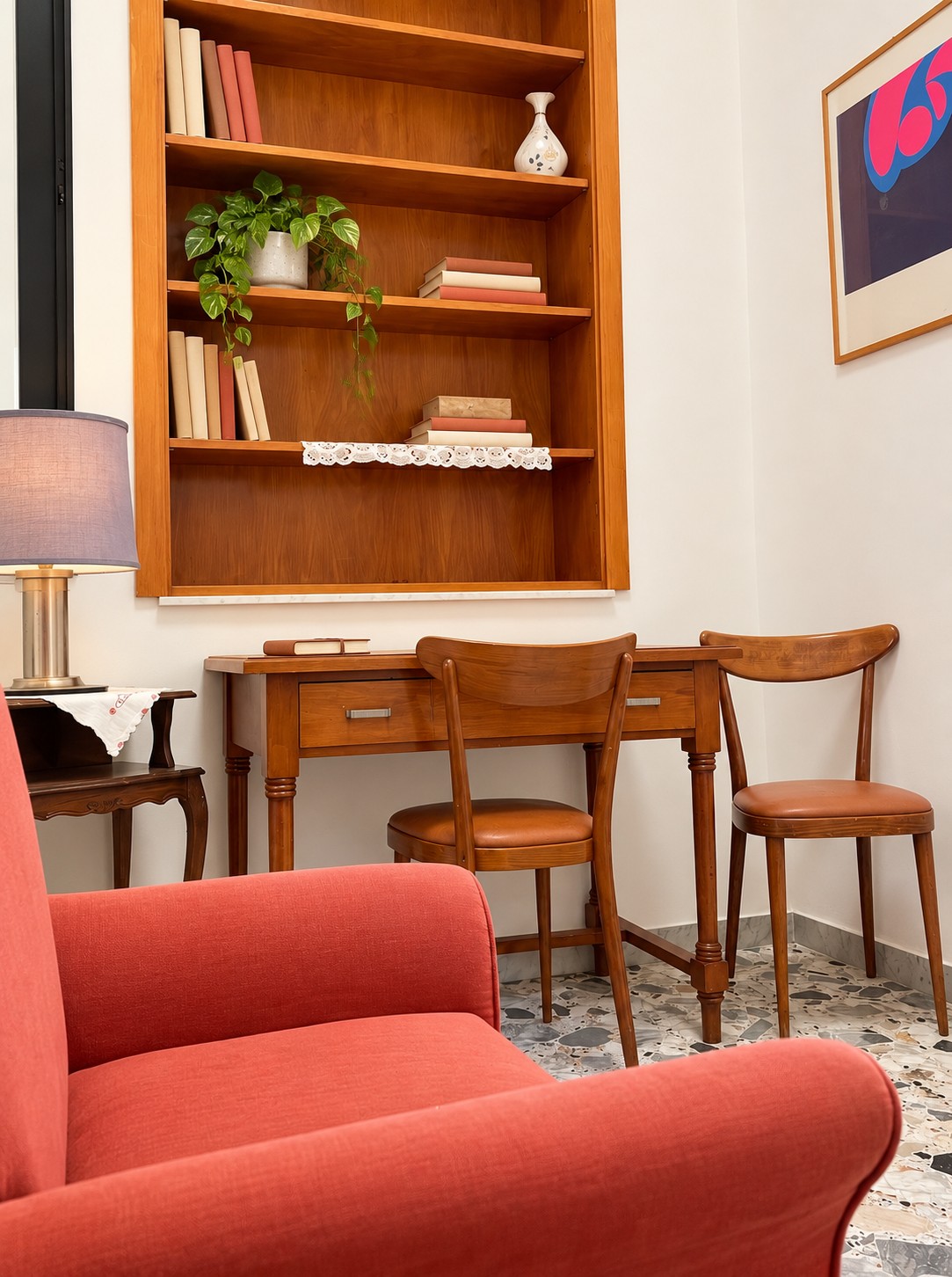 Angolo lettura con poltrona color corallo, scrivania in legno e libreria a muro