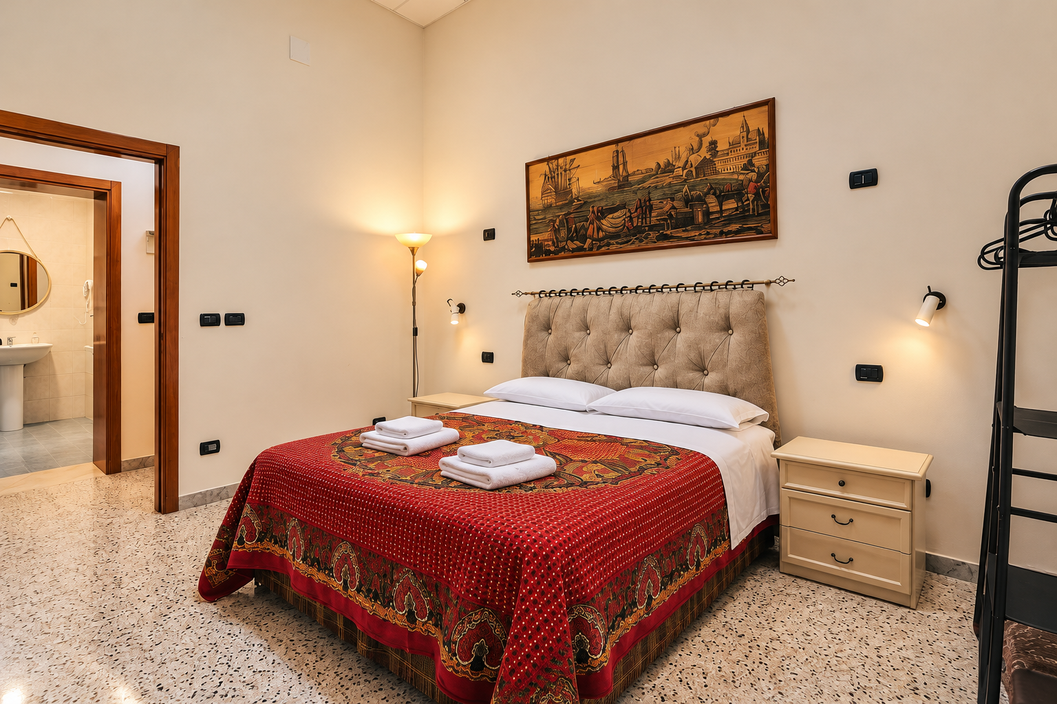 Camera matrimoniale con pareti color crema, testiera imbottita e coperta rossa con bordo decorato